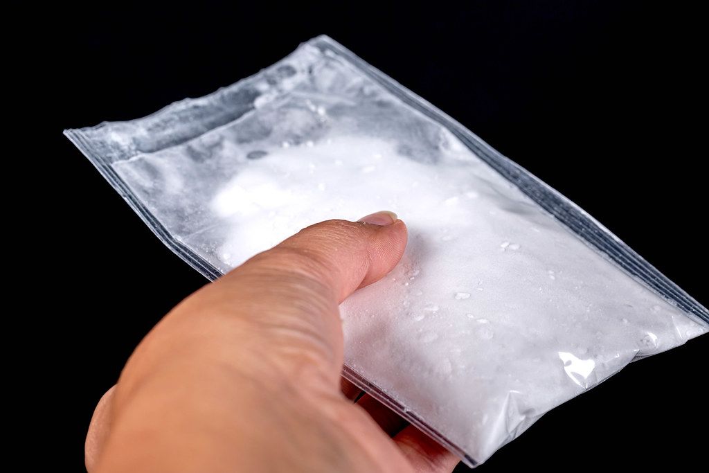 Bag with white powder in hand on a black background. The concept of drug addiction