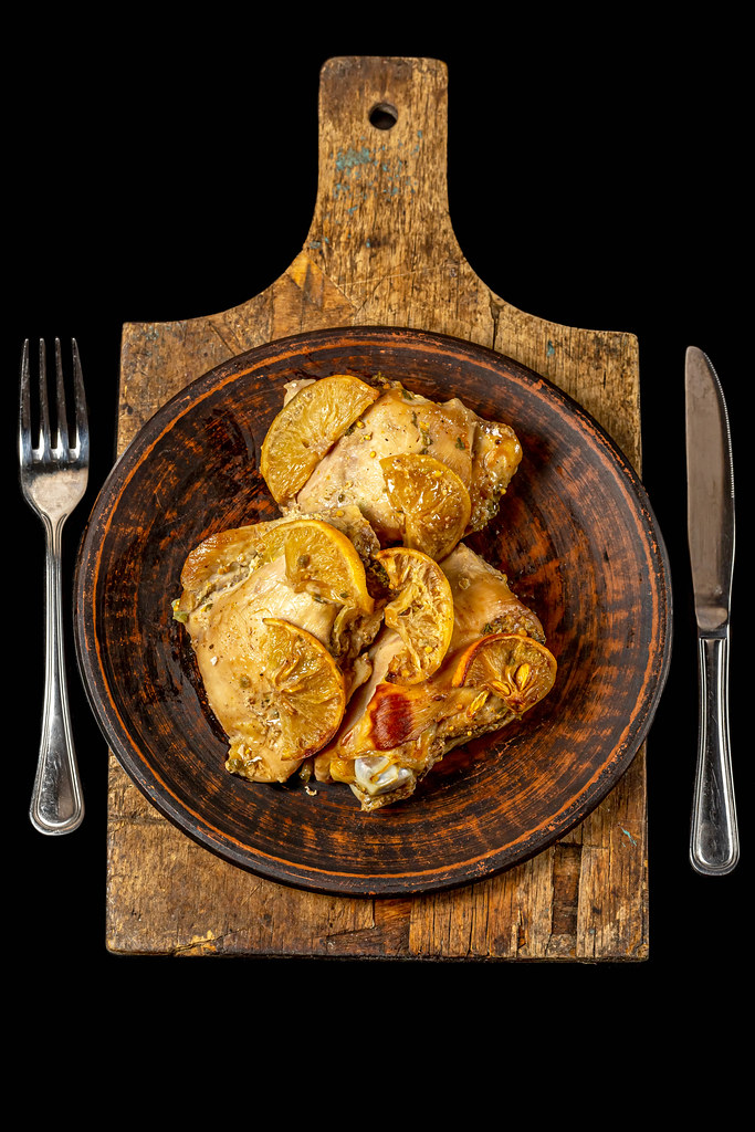 Baked chicken pieces with lemon on an old cutting board, dark background