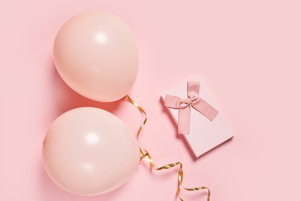 Balloons and present box on pink background