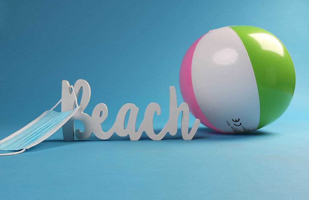Beach ball with medical face mask and beach text on blue background