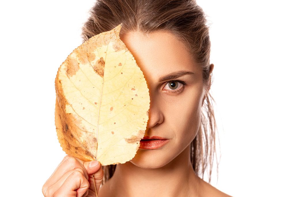 Beautiful girl holding an autumn leaf near her face