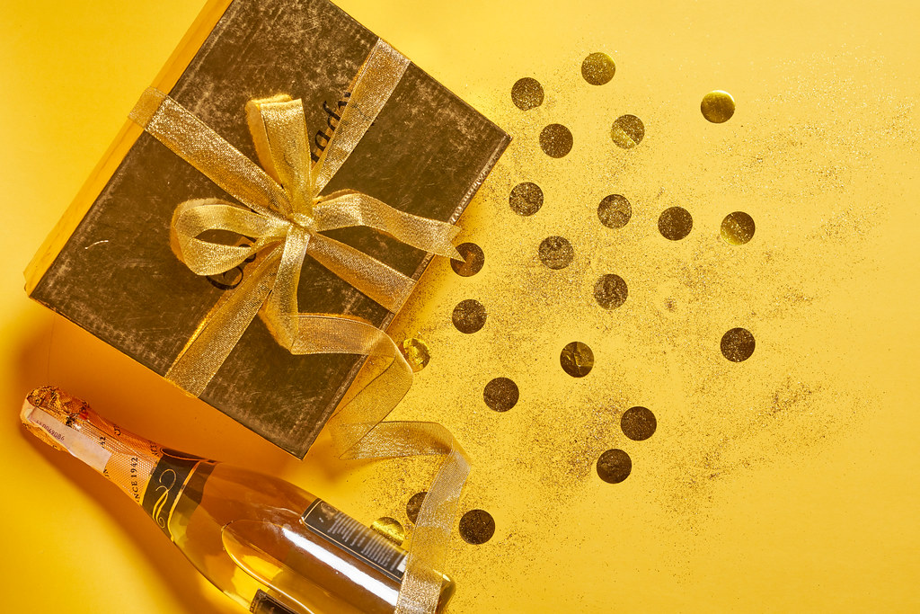 Birthday gift, festive confetti and champagne bottle on yellow background