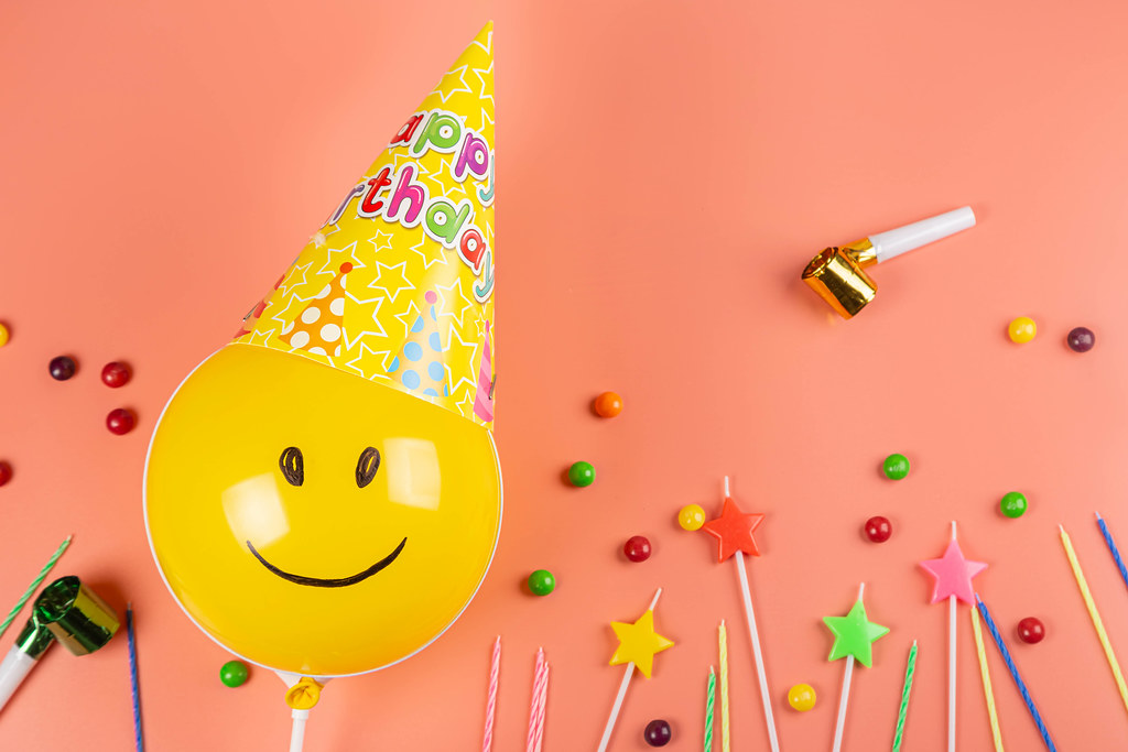 Birthday party background with balloon in a cone hat on pink background