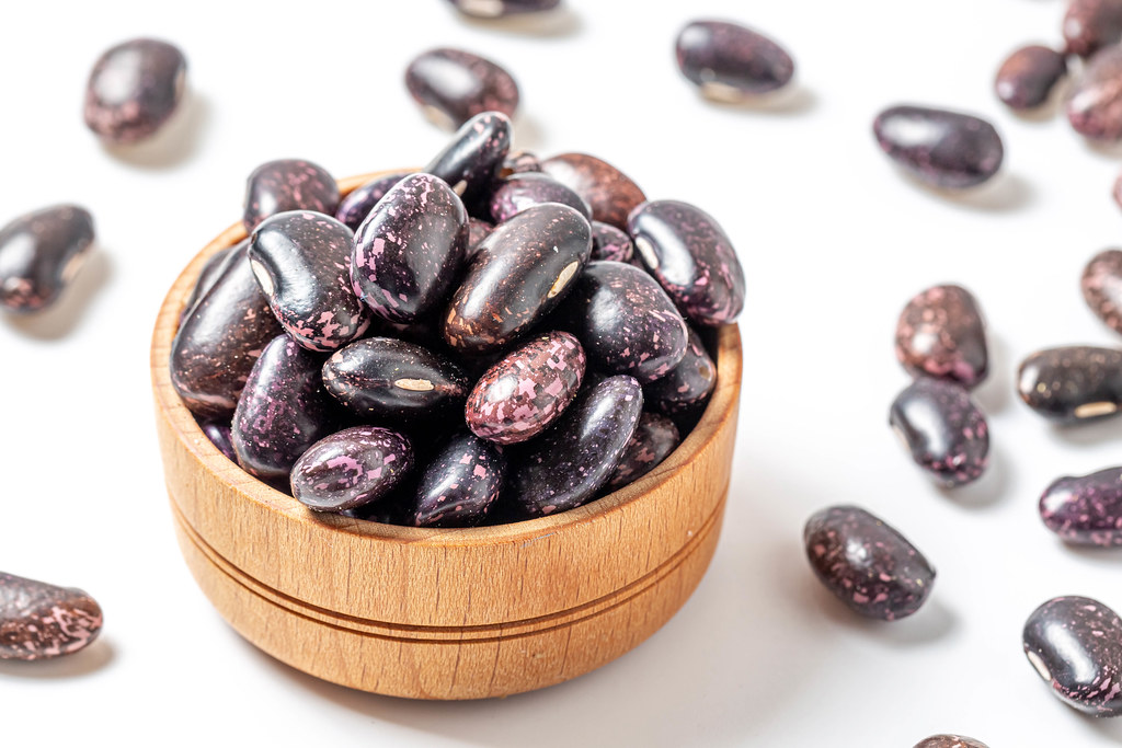 Black beans in a wooden bowl on white and scattered beans
