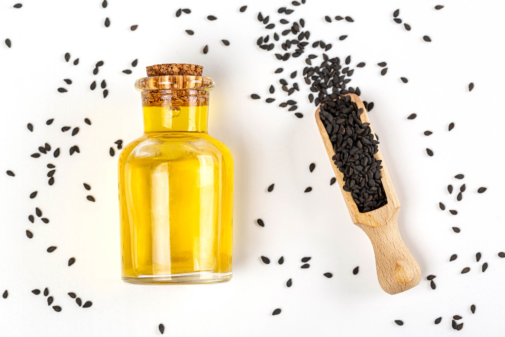 Black sesame seed and a bottle of sesame seed oil over white background, top view
