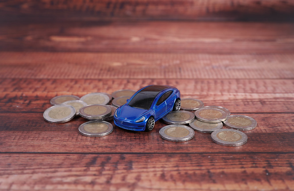 Blue electric car with coins on wooden table