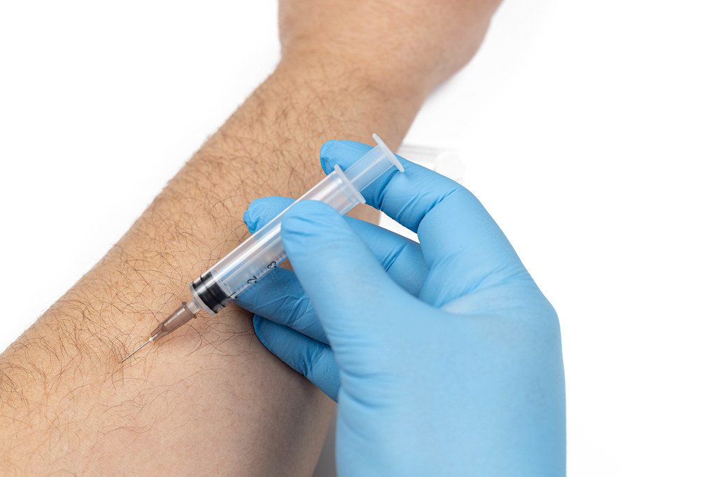 Blue gloves on the hand with injection in the arm