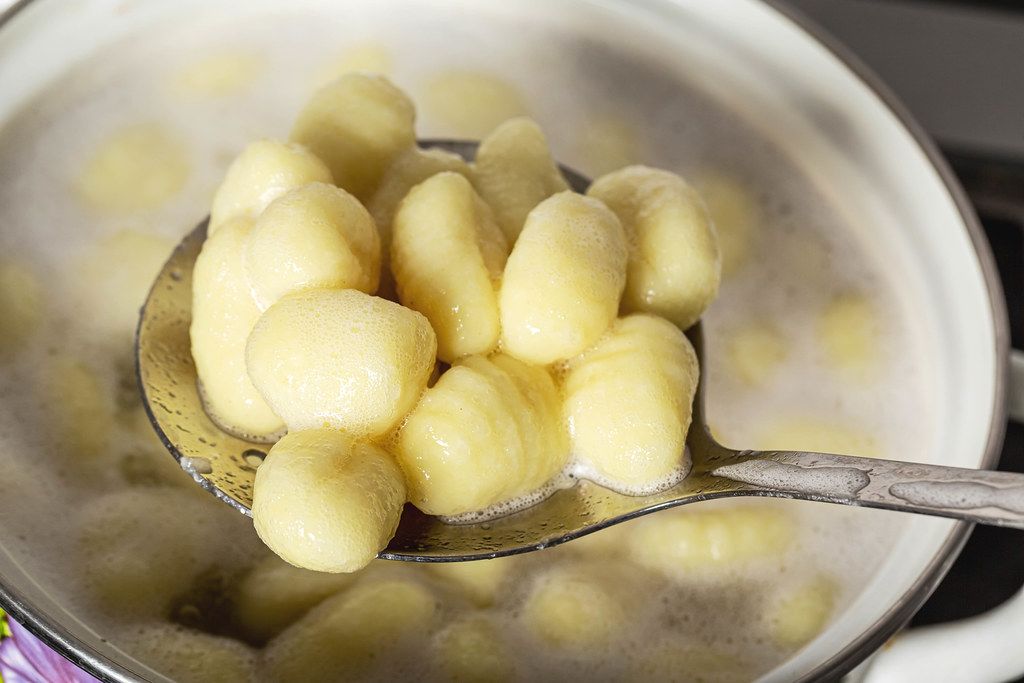 Boiled potato gnocchi on a slotted spoon get out of a pot of boiling water