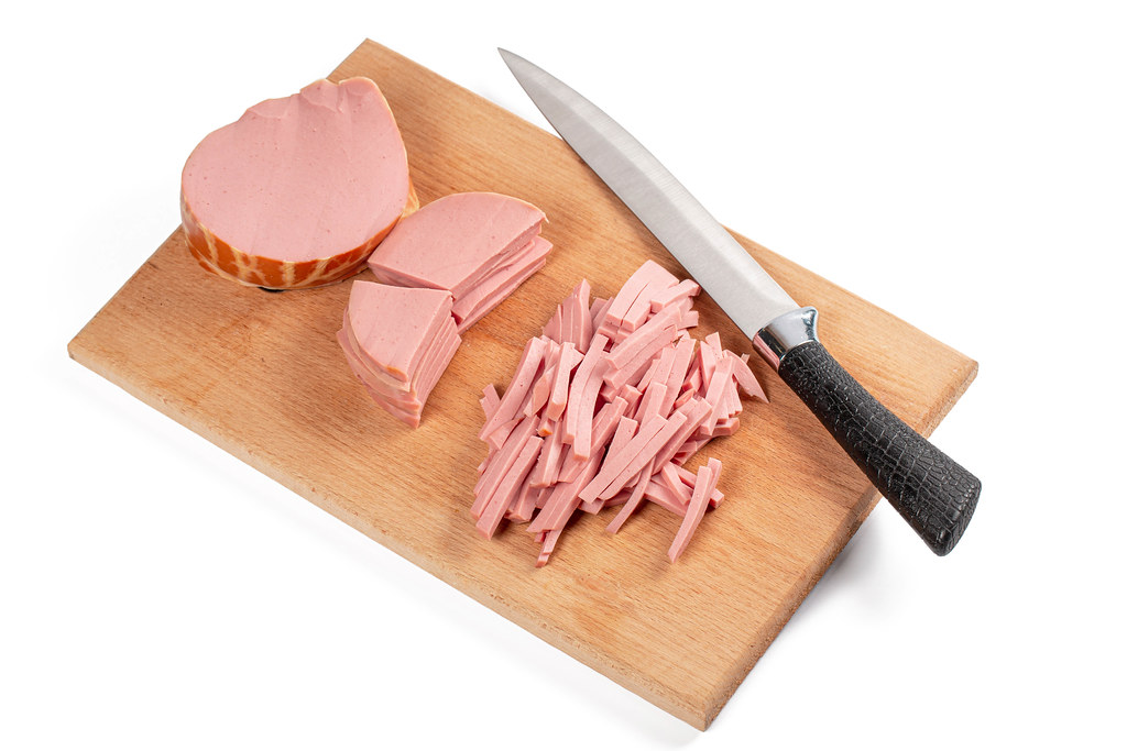 Boiled sausage sliced on a kitchen board with a knife