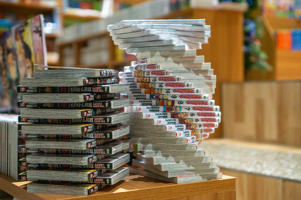 Bokeh Photo of Spiral of Manga Books of the Series Naruto next to a Stack of Comic Books in a Bookstore