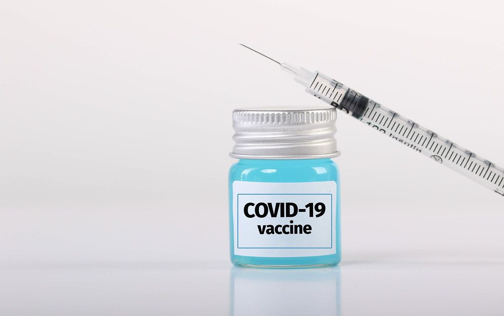 Bottle with Covid-19 vaccine and syringe on white background