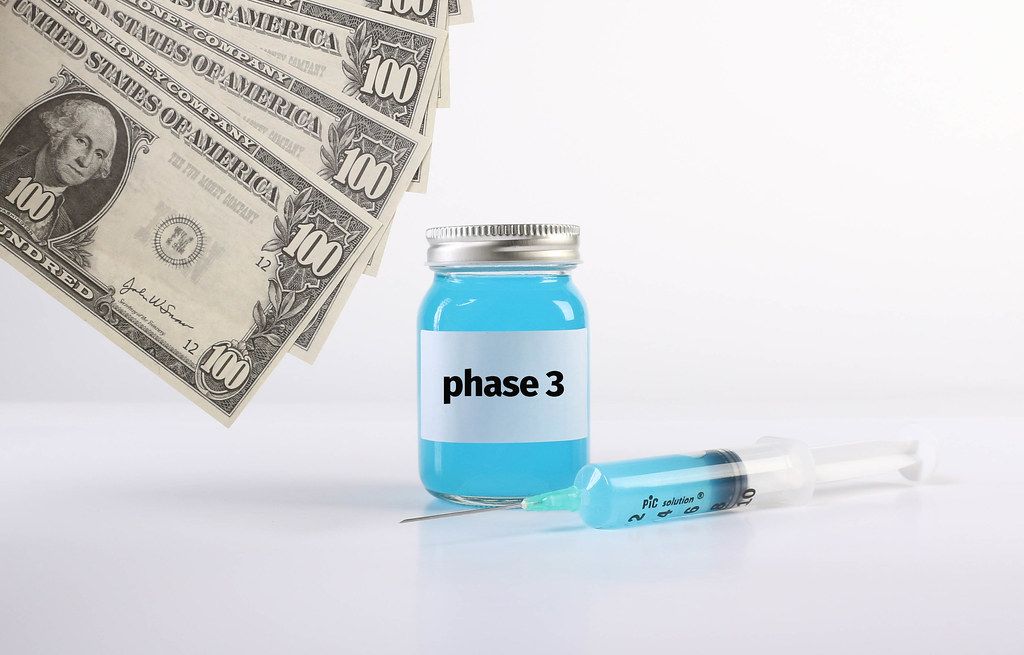 Bottle with Phase 3 text with money and syringe on white background