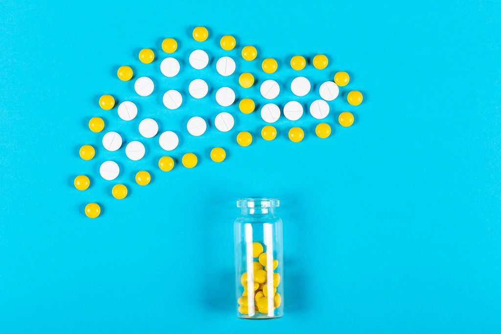 Bottle with scattered yellow pills and liver from pills on blue background