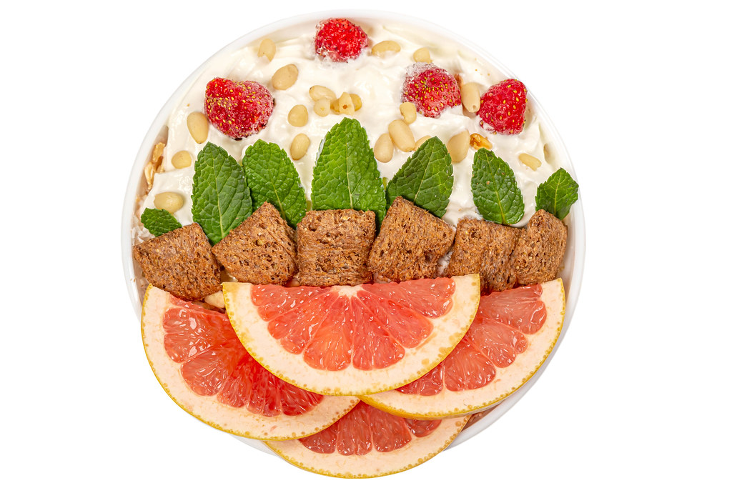 Bowl of oatmeal with grapefruit pieces, strawberries, mint, whipped cream and pine nuts, top view