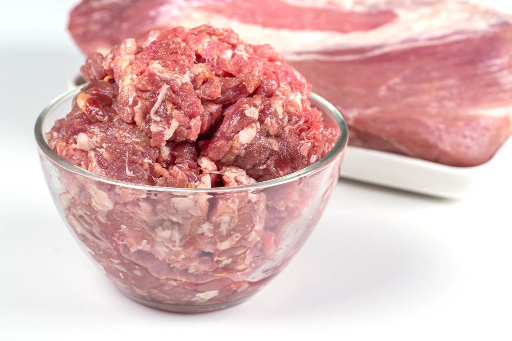 Bowl of raw minced meat and fresh pork meat on white background