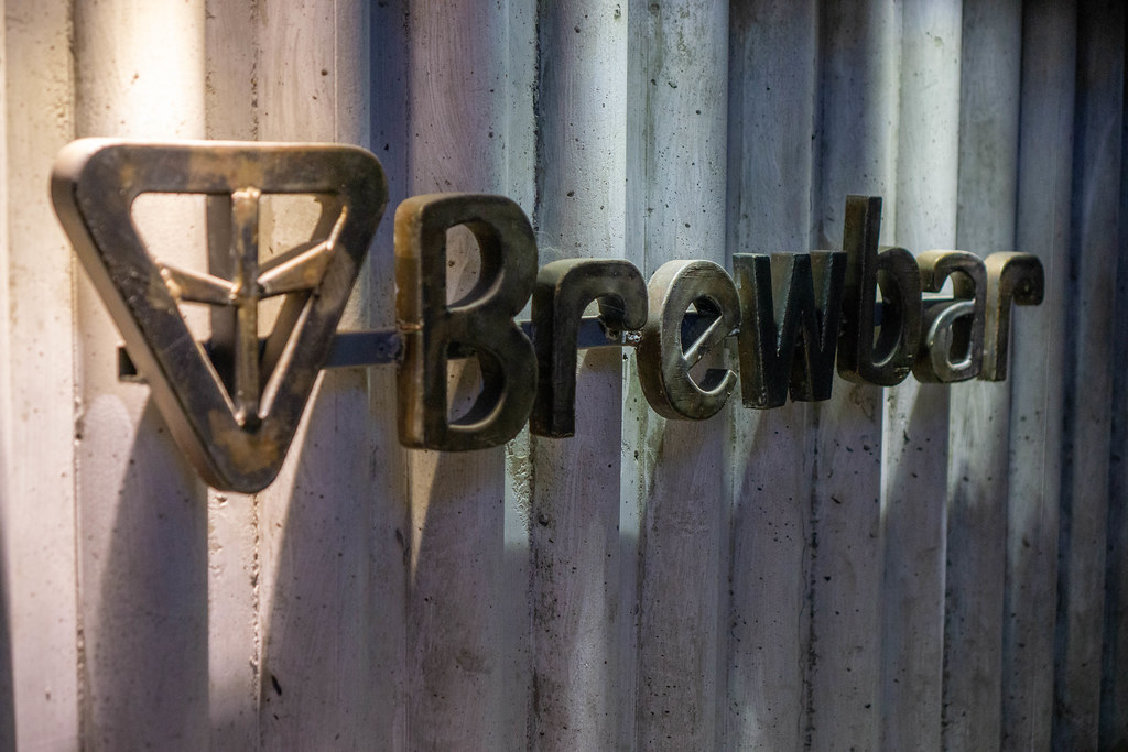 Brewbar Steel Brand Logo with Letters on a Cafe Wall with Lamps pointing on it
