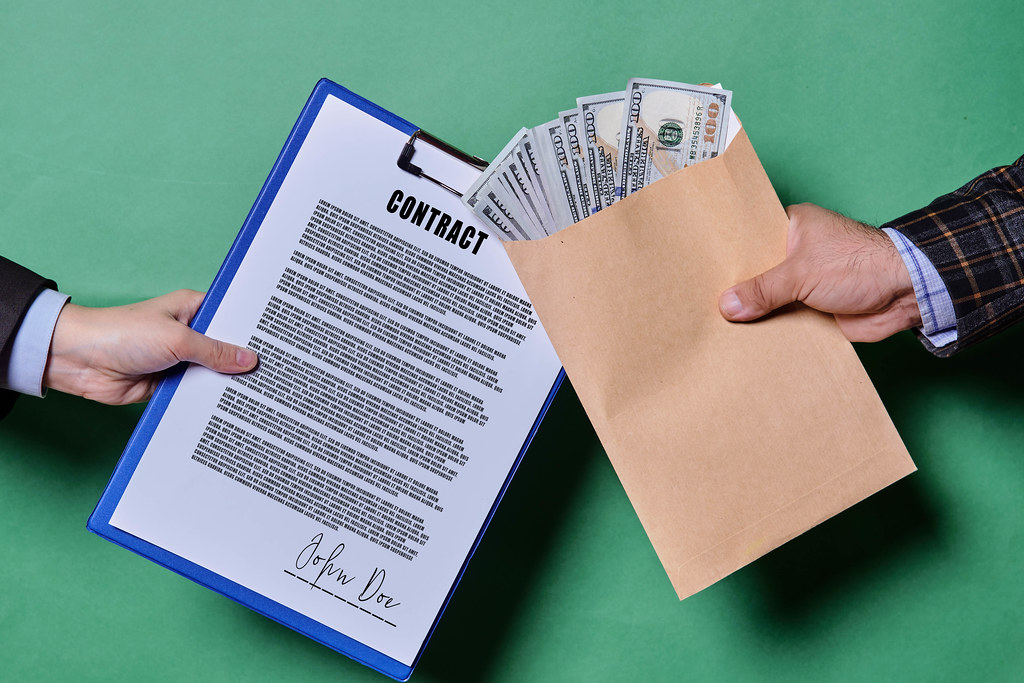 Bribery and corruption concept. A person giving money in the envelope for signing a contract