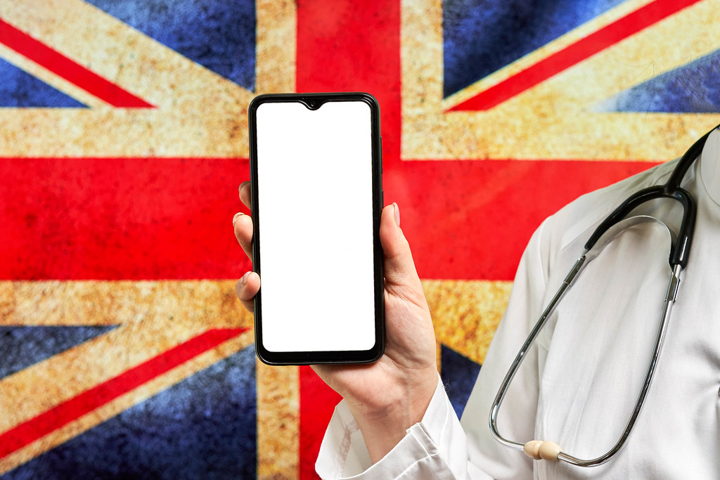 British doctor holds smartphone against flag