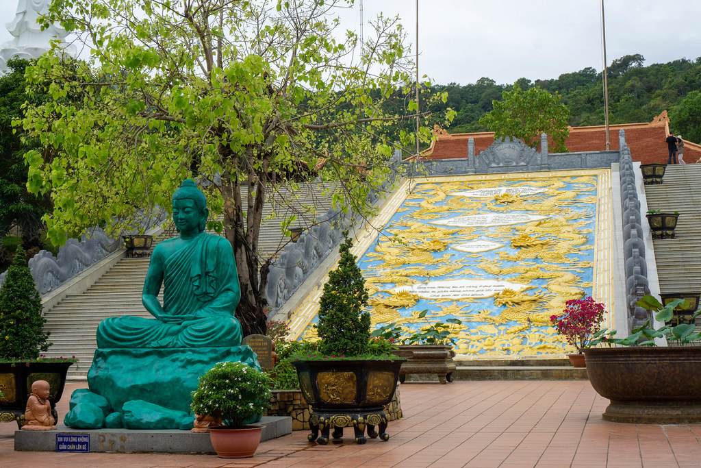 Buddha Statue mit Bäumen und Pflanzen vor einer großen goldenen Drachen Verzierung am Ho Quoc Tempel in Phu Quoc, Vietnam