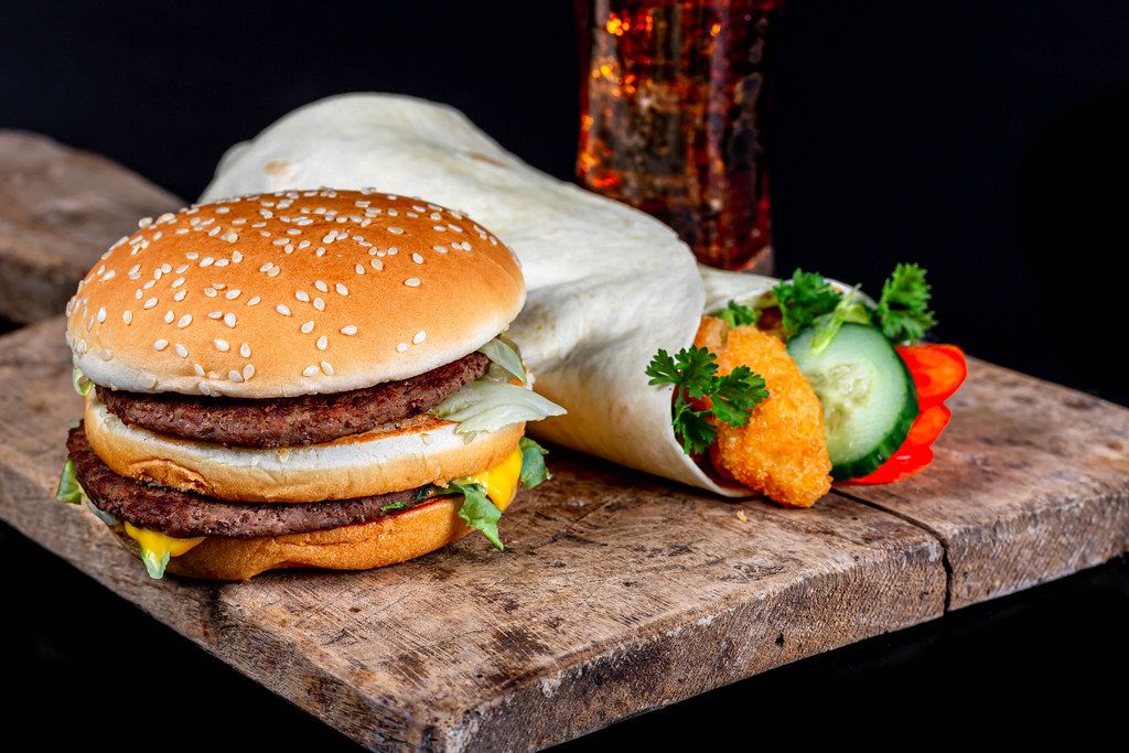 Burger, shrimp roll and Coca Cola on old wooden kitchen board