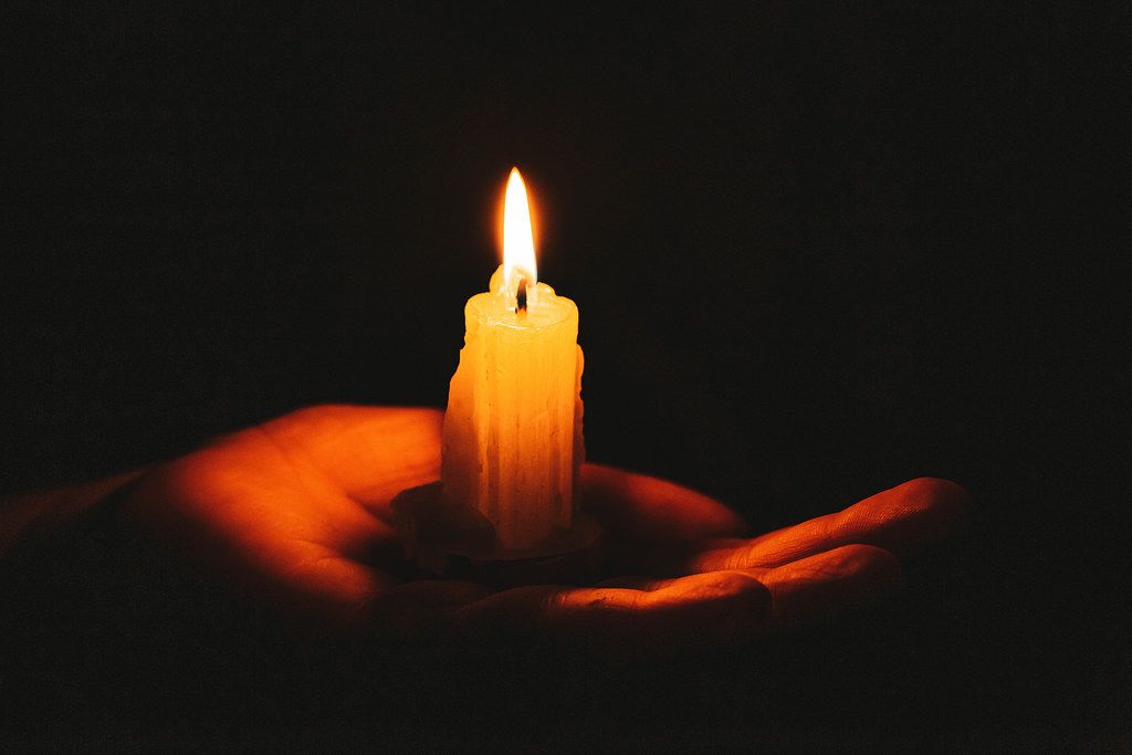 Burning candle on a female hand, dark background. Symbol of life, love and light
