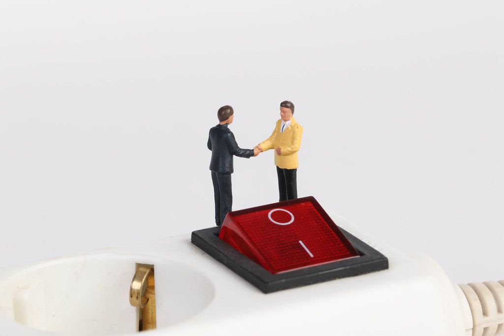 Businessman shaking hands on white electric splitter with red switch