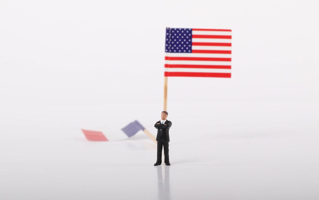 Businessman standing in front of flag of USA and fallen flag of France