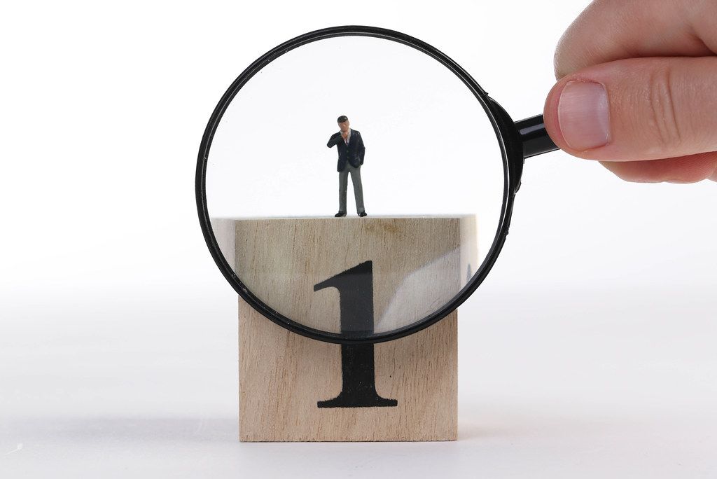 Businessman standing on top of wooden cube with big number 1 and magnifying glass