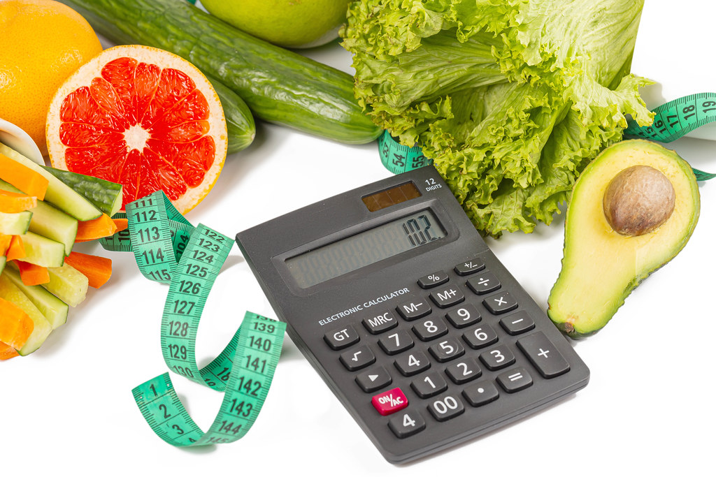 Calculator, fresh vegetables and fruits on a white background with a measuring tape