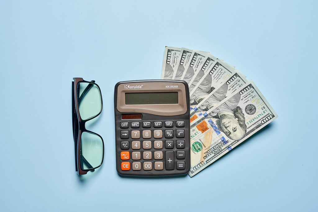 Calculator, us dollars and eyeglasses on bright blue background