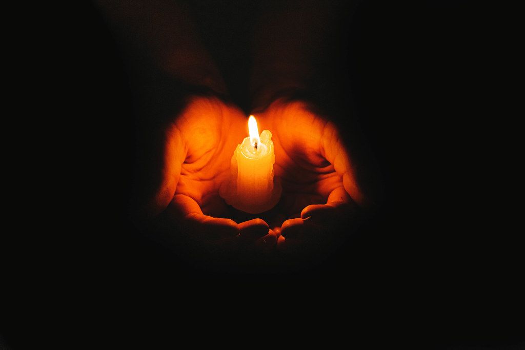 Candle flame glowing on a dark background in women hands. The concept of mourning, memory and hope