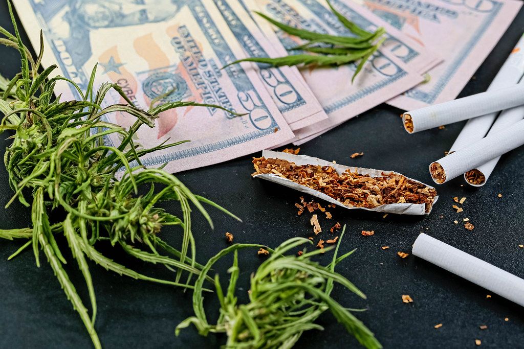 Cannabis herb with money and cigarettes on black