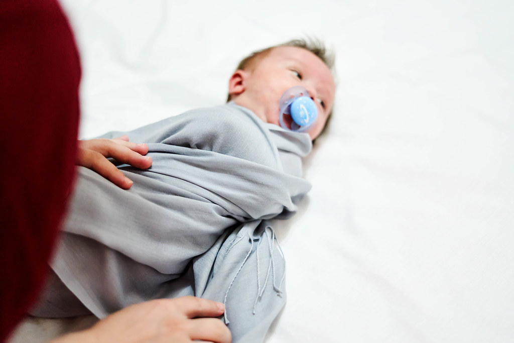 Caring mother wrapping her little 1-month-old baby boy with blanket on changing table