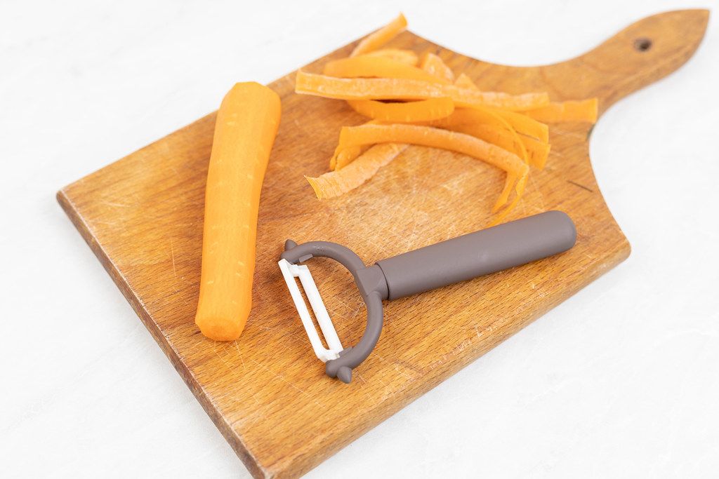 Ceramic peeling knife with peeled carrot on the wooden board