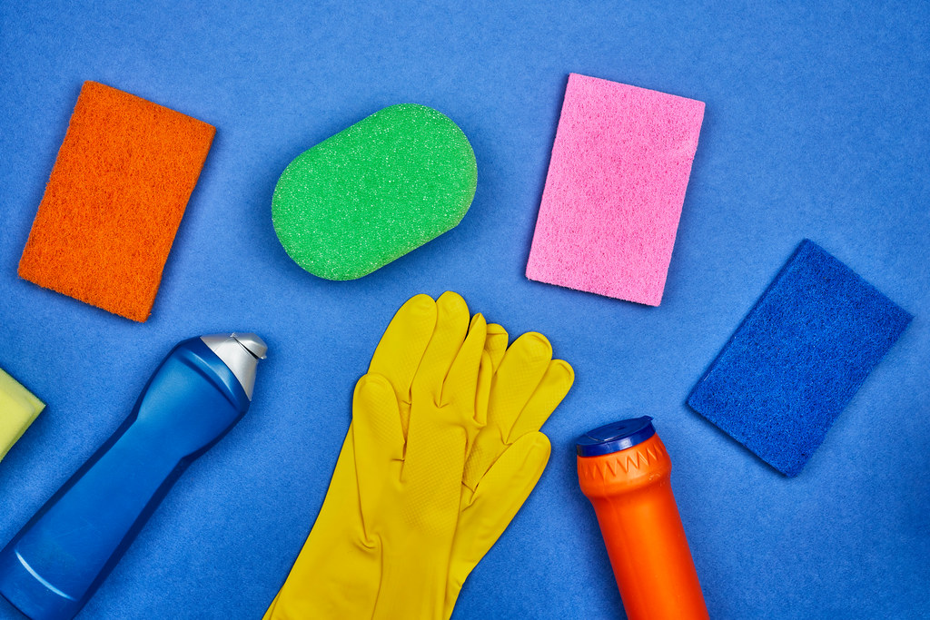 Chemical cleaning supplies bottles and different sponges on blue background