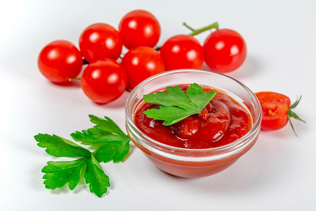 Cherry tomatoes and sauce in a glass bowl on a white background