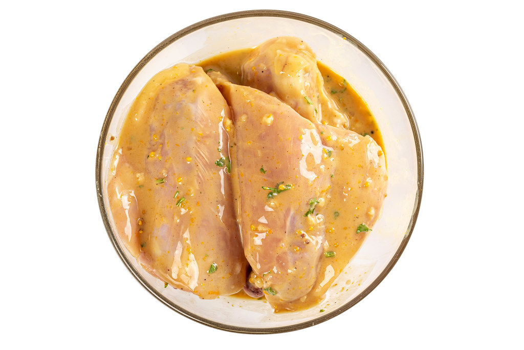 Chicken meat with marinade in a glass bowl, top view