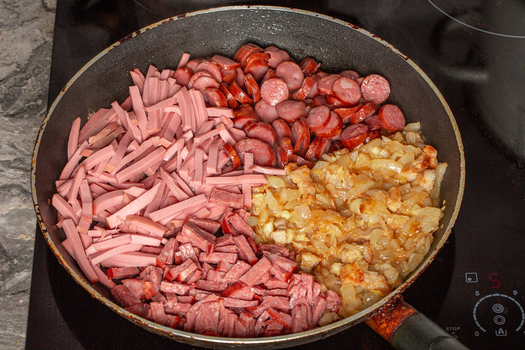 Chopped sausages and onions are fried in a skillet