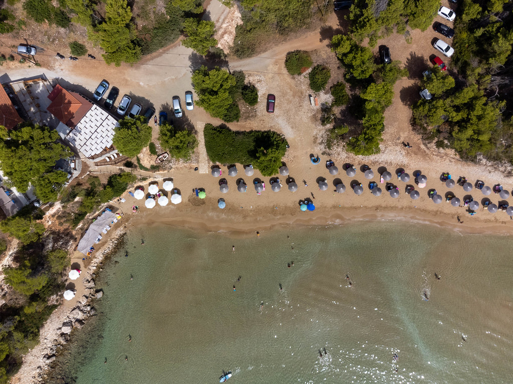 Chrisi Milia: der einzige Sandstrand auf Alonissos. Schmaler Strand mit zwei Reihen von Sonnenschirmen