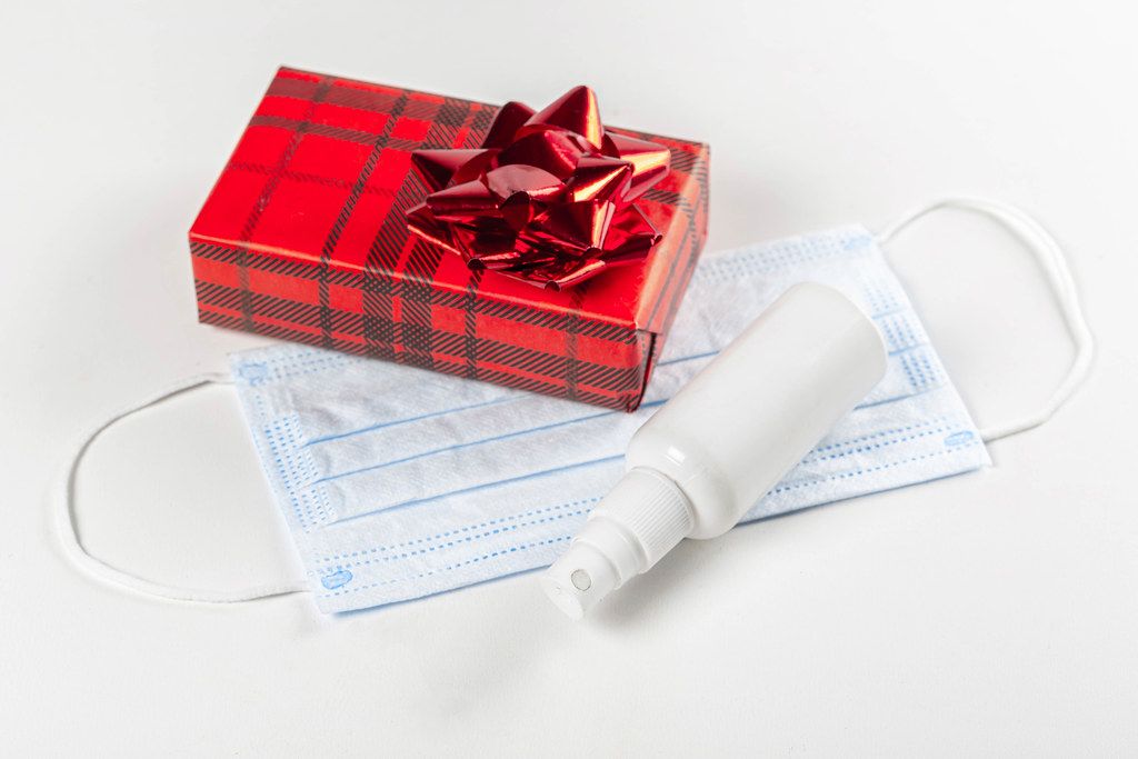 Christmas gift with face mask and antiseptic on a white background. Personal protection concept during the holidays