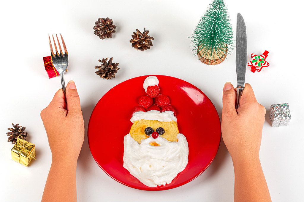 Christmas Santa pancake with berry for kid breakfast on white background and hands with knife and fork