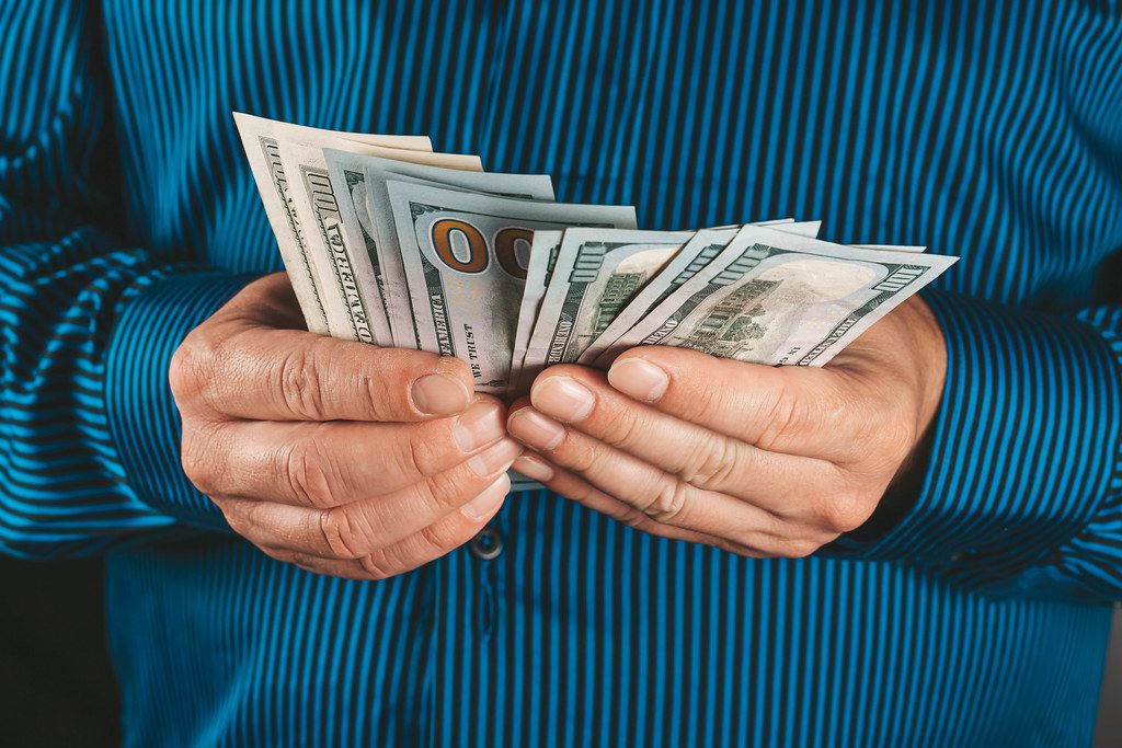 Close-up, a man with a blue shirt holds dollars in his hands