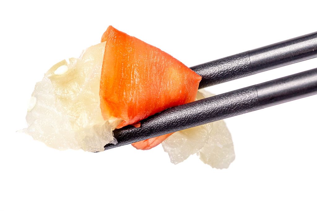 Close-up, a piece of raw fish with pickled ginger in black chopsticks