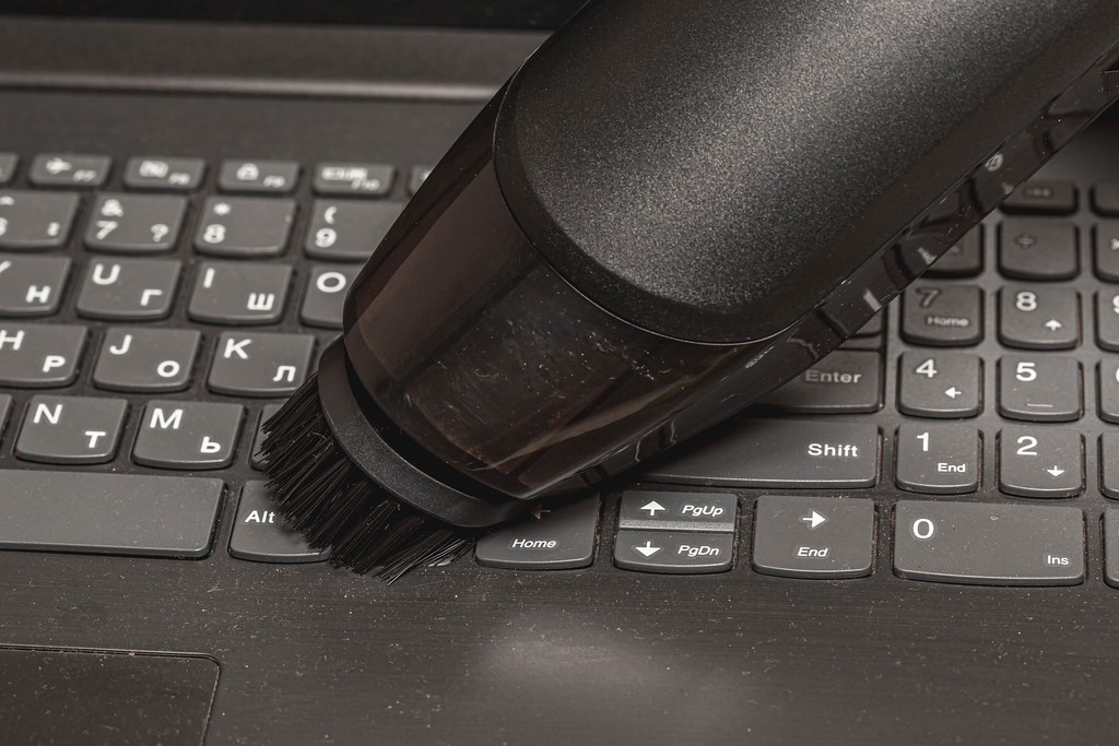 Close-up, a portable vacuum cleaner with a brush attachment collects dust on the keyboard