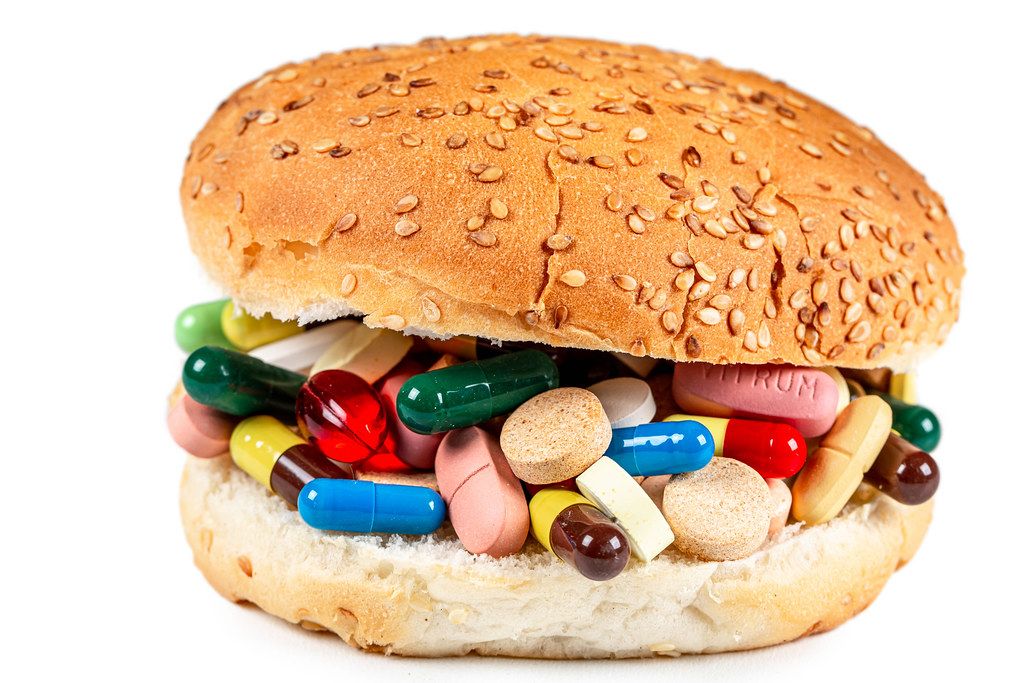 Close-up burger with medicines and pills inside on white