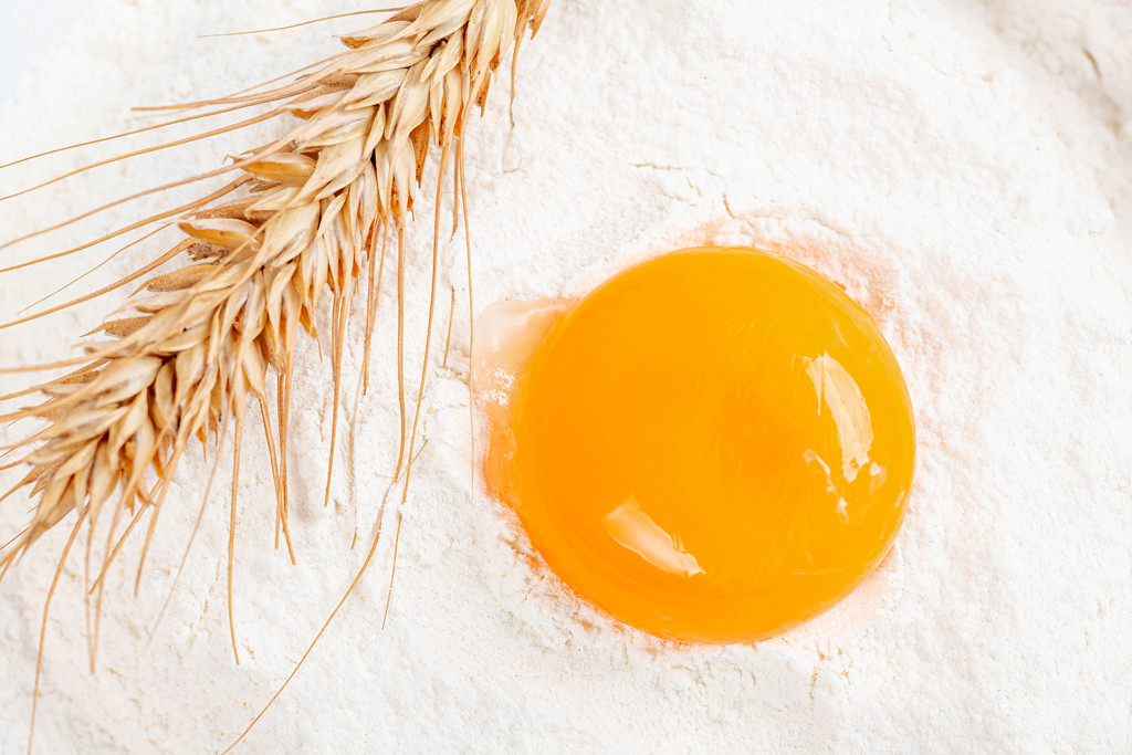 Close-up, egg yolk and a spike of wheat on flour