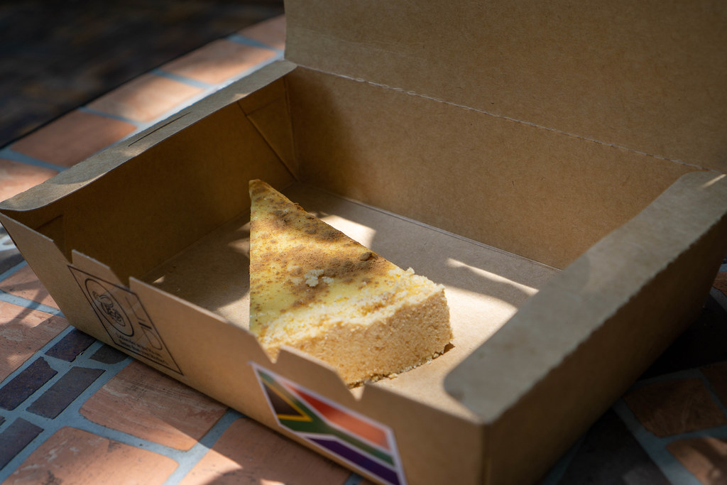 Close Up Food Photo of a Slice of Cheesecake in an Environment-Friendly Take-Away Paper Box on a Garden Table in the Sun