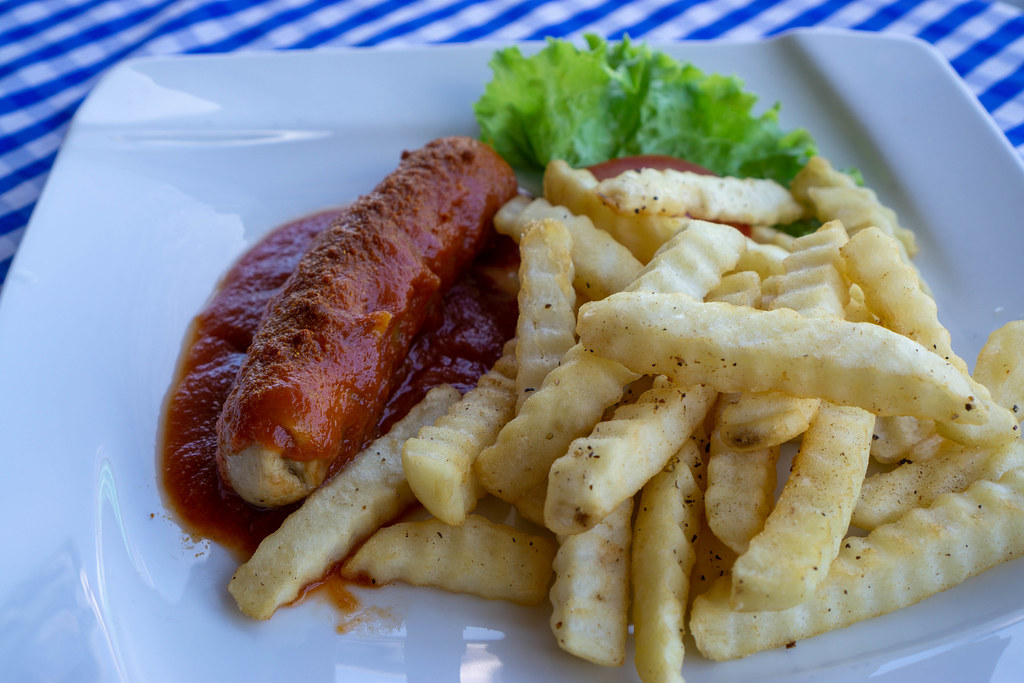 Close Up Food Photo of German Currywurst Sausage with Curry Powder, Tomato Ketchup and French Fries with Salt and Pepper on a White Plate