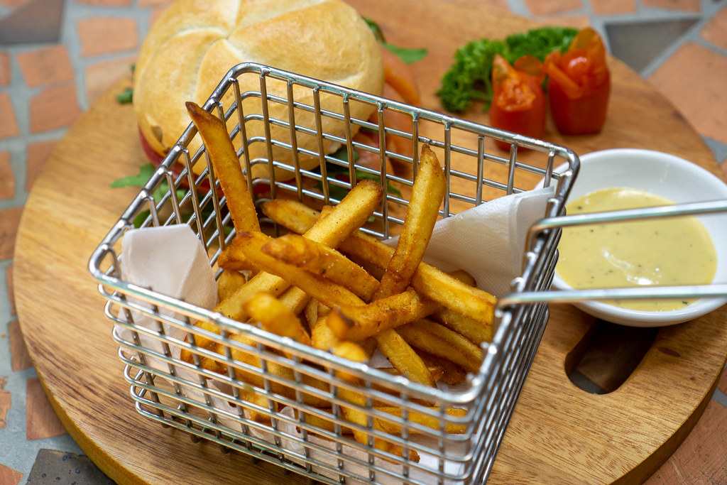 Close Up Food Photo of Homemade French Fries in a Metal Basket on a Wooden Tray with Smoked Salmon Sandwich and Honey Mustard Sauce in a Restaurant
