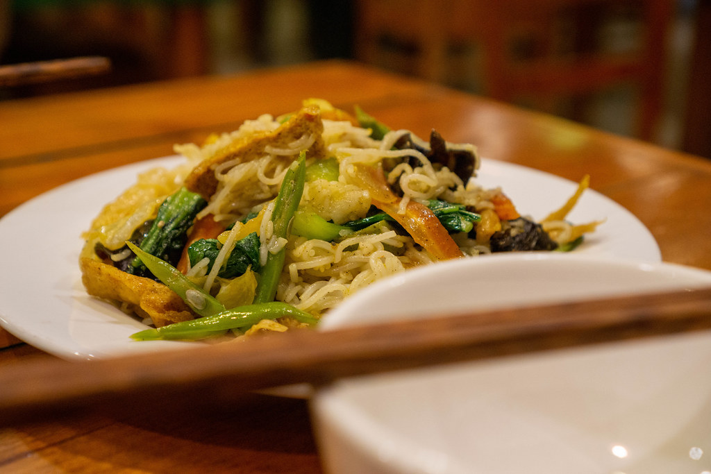 Close Up Food Photo of Stir Fried Noodles with Green Beans, Fried Tofu, Mushrooms, Carrots and Bok Choy on a Wooden Table in a Restaurant